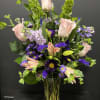 Tall vase arrangement of pink roses and lilies with purple flowers and green spikes.