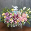 Pastel flower arrangement with lilies, roses, and a ceramic bunny in a metal container.