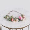 Delicate floral crown with pink and white roses arranged along a vine base on a marble table.