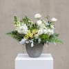 Low white and green floral arrangement with orchids and round white blooms in a gray pot.