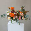 Low arrangement of orange marigolds and blush roses in a white bowl vase on a white pedestal.