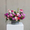 Low arrangement of pink, purple, and red roses and carnations in a round metal container