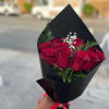 Handheld bouquet of red roses with white filler flowers wrapped in black paper and red ribbon