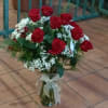 Arrangement of red roses with white filler flowers in a clear glass vase tied with a sheer bow.