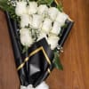 Wrapped bouquet of white roses with baby's breath in black paper with gold trim and white ribbon.