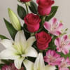 Tall arrangement of red roses, white lilies, and pink blooms in a wooden box with a burlap bow