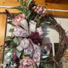 Grapevine wreath with pink peony blooms, greenery, and large white and burgundy patterned bow.