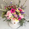 Colorful arrangement of pink gerberas, roses and mixed blooms in a white round vase with tall pussy willow branches