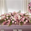 Pink and white casket spray with lilies, roses, carnations, and hydrangeas on a mauve casket