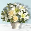 White lilies and cream roses in a white vase with blue hydrangeas