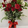 Tall arrangement of red roses and carnations with white blooms in a red vase with a red bow