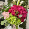 Bright pink roses, green hydrangeas, and pale pink blooms arranged in a clear glass vase with ribbon