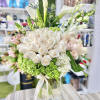 Tall arrangement of white roses, calla lilies and green hydrangeas in a clear glass vase