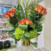 Tall arrangement of orange roses, white calla lilies, and green hydrangeas in a clear glass vase
