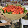 Large bouquet of orange and red roses wrapped in patterned brown paper and cellophane