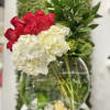 Asymmetrical arrangement of red roses and white hydrangeas in a round clear glass bowl vase