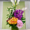 Tall modern arrangement with yellow roses, purple orchids, white calla lilies, and pink hydrangea in a glass cube vase