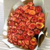 Large wrapped bouquet of tightly clustered orange and red roses on a wooden surface