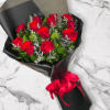 Bouquet of red roses with white filler flowers wrapped in black paper and tied with a red ribbon