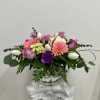 Low glass vase arrangement with pink gerbera daisies, purple roses, white tulips, and green hydrangea
