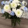 Tall vase arrangement of white mums, blue carnations, and pale roses with ferns.