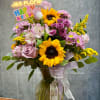 Mixed bouquet with sunflowers, pink roses, and purple blooms in a glass vase