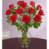 Arrangement of red roses with white filler flowers in a clear glass vase on a dark table