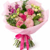 Hand-tied bouquet of pink roses, mums, and mixed blooms wrapped in pink paper with a satin bow.