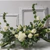 Long low arrangement of white roses, lilies, and hydrangea with tall green accents