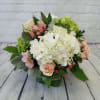 Low arrangement of white hydrangeas with peach roses and pink accents in a green glass cube vase