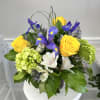 Compact arrangement of yellow roses, purple irises, green hydrangeas, and white alstroemeria in a glass vase