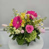 Bright mixed arrangement with hot pink gerbera daisies, pink rose, tulips, and yellow blooms in a clear glass vase