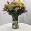 Mixed bouquet of yellow lilies, peach roses, and pink blooms in a clear vase with a raffia tie