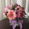 Compact pink and purple flower arrangement in a clear glass cube vase with a lavender ribbon bow