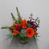 Bright mixed arrangement with orange gerbera, lilies, roses, and succulents in a clear glass vase