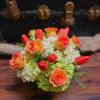 Low arrangement of orange roses and tulips with pale green hydrangeas in a glass vase