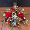 Low event centerpiece with red roses, white filler blooms, metallic foliage, and wheat accents.