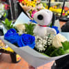 Bouquet of blue and white roses with baby's breath and a Snoopy plush toy wrapped in light paper