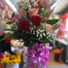 Tall vase arrangement of red and pink roses, pink lilies, and baby's breath with a large purple ribbon bow.
