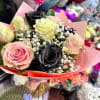 Hand-tied bouquet of pink, cream, and black roses with white filler flowers in pink wrap