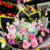 Hand-tied bouquet of pink roses and sprays with blue and white hydrangeas in decorative wrap
