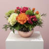 Bright orange, pink, and white flowers in a low hammered copper bowl vase on a white pedestal
