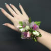 Wrist corsage with small white and pink roses and purple accents on a person’s arm