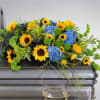 Casket spray of yellow sunflowers and blue hydrangeas with green accents on a silver casket