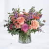 Mixed bouquet of peach and lavender roses with purple accents in a clear glass vase