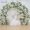 Large white rose wedding arch with matching floral frame beside a mannequin in a bridal gown and chair.