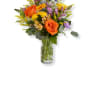 Tall mixed bouquet with orange roses, yellow and purple flowers in a clear glass vase