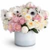 Low pastel arrangement of pink and cream roses with white anemones in a white cylinder vase