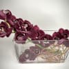 Horizontal arrangement of deep purple cymbidium orchids in a clear rectangular glass vase.