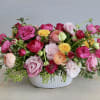 Low centerpiece of bright pink, yellow, and peach blooms in a white ceramic bowl.